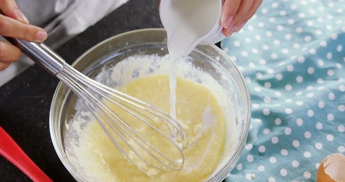 Woman adding milk to beaten eggs in a bowl 