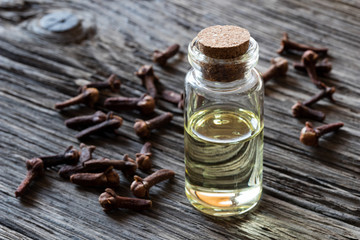 A bottle of clove essential oil with dried cloves on a wooden background