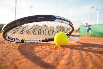 Close-up tennis racket and ball placed on court ground while player hitting ball.  