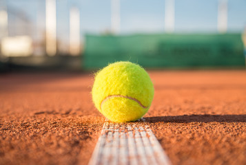 Small tennis ball lying on white line on tennis court on sunny day. 