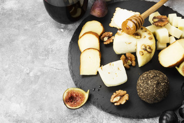 Fototapeta na wymiar Snacks with wine - various types of cheeses, figs, nuts, honey, grapes on a gray background. Copy space. Food background