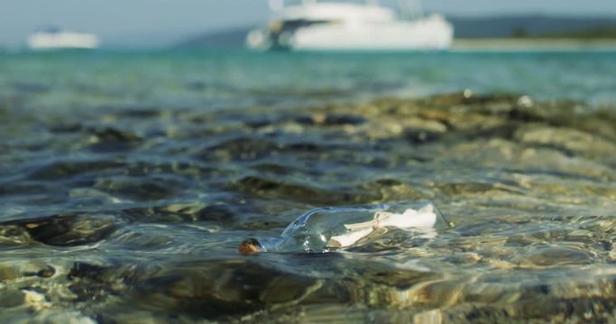 Close-up Shot of a Message in the Bottle, Drifting in Shallow Seas with White Yacht in the Background. Shot on RED Epic 4K UHD Camera.