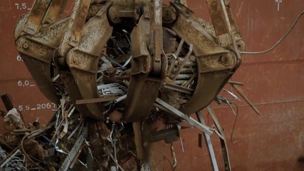 huge industrial grapple is moving captured scrap metal and throwing it down, for sorting in a big rubbish dump
