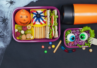 Halloween lunch box with school lunch with sandwich, fruits, vegetables on black background with blank space for text