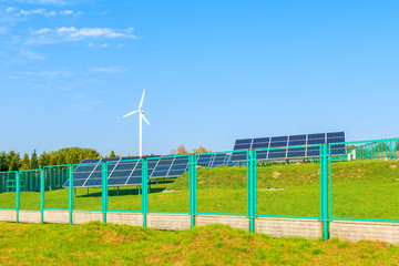 Solar panels on green field with wind turbine in background, Poland