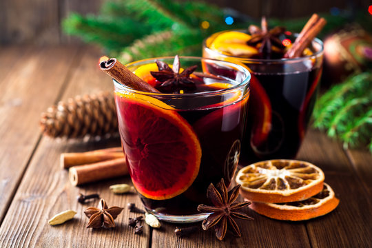 Two glasses of christmas mulled wine with oranges and spices on wooden background.