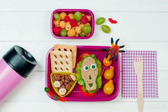 Open Halloween lunch box with school lunch near thermo mug and fork