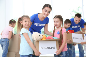 Happy volunteers with children holding donation boxes indoors