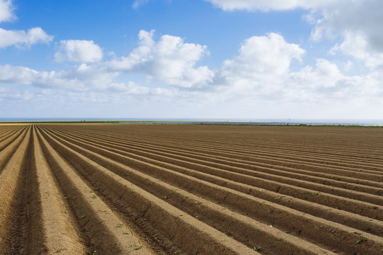 Plowed agricultural fields prepared for planting crops in Normandy, France. Countryside landscape with cloudy sky, farmlands in spring. Environment friendly farming and industrial agriculture concept.