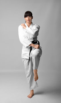 Young woman practicing karate on light background