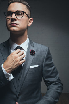 An elegant young man adjusting his tie looking away