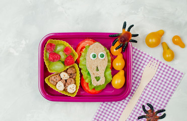 Open Halloween lunch box with school lunch with skull shape sandwich on grey concrete background