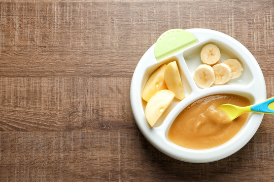 Section Plate With Baby Food And Fresh Fruits On Wooden Background