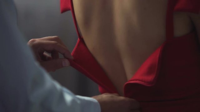 Male lover slowly unzipps red dress from behind, unveiling bare female back