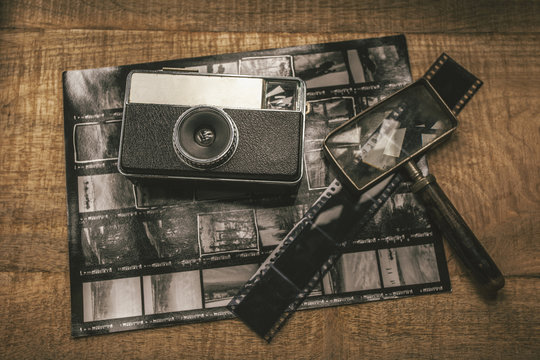 Old analog camera, film, magnifying glass and contact sheet over wooden table.