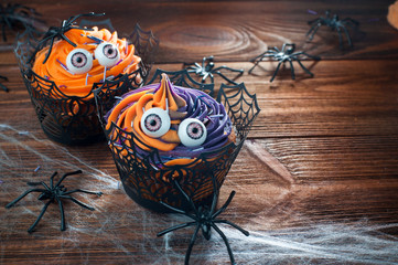 Two Halloween cupcakes on rustic wooden table covered with web