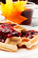 A cup of tea and crispy wafers./A cup of tea and crispy wafers poured with raspberry jam. White dishes. White background.