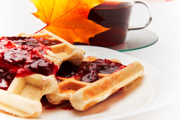 A cup of tea and crispy wafers./A cup of tea and crispy wafers poured with raspberry jam. White dishes. White background.