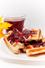 A cup of tea and crispy wafers./A cup of tea and crispy wafers poured with raspberry jam. White dishes. White background.