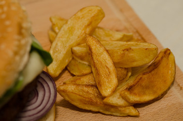Delicious homemade hamburger served with French fries on wooden background. Delicious burger with onion, tomato, cheese and lettuce. Fast food meal. Rustic style.