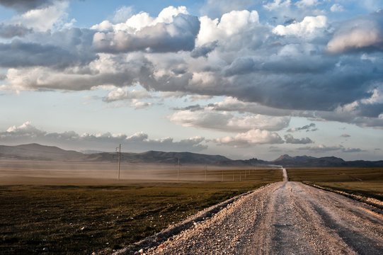 Dirt road in a prairie to the mountains of kyrgyzstan at sunset
