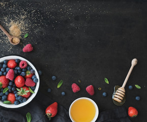 Berry frame with copy space. Strawberries, raspberries, blueberries and mint leaves, honey, cane sugar, dark grunge background, top view, copy space