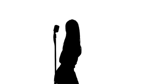 Woman sing song and dances near a retro microphone. Silhouette. White background. Slow motion