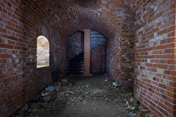 Fototapeta na wymiar Arched corridor of the old Prussian fortress of red brick, ending with a spiral staircase