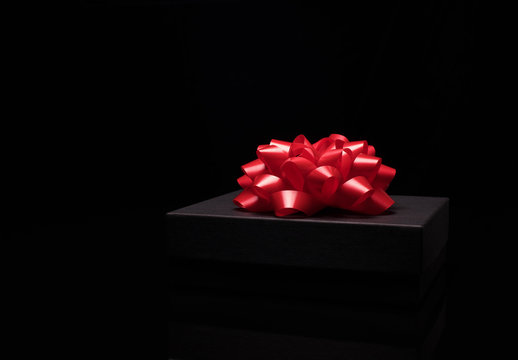 Black gift box on a black surface with big red bow. Close up. Celebrate concept, New Year, Merry Christmas, Anniversary,Birthday,Valentines day,men,women, winter holidays.