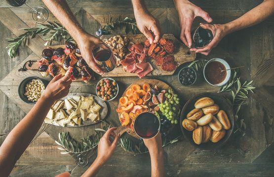 Flat-lay of friends hands eating and drinking together. Top view of people having party, gathering, celebrating together at vintage wooden rustic table set with different wine snacks and fingerfoods