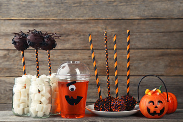 Sweet halloween cake pops with cocktail in plastic cup on grey background