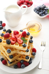 Sweet waffle with berries, milk and honey on white wooden table