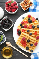 Sweet waffle with berries, milk and honey on black wooden table