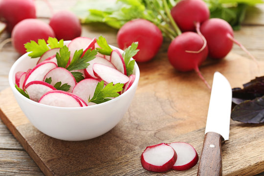 Sliced red radish in bowl on brown cutting board