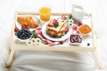 Tasty breakfast in bed on wooden tray