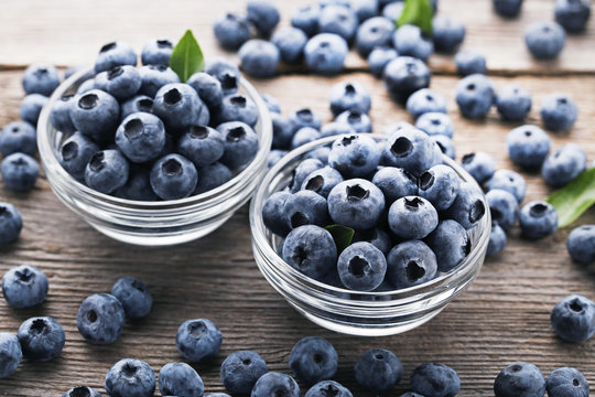 Ripe blueberries in glass bowls on wooden table