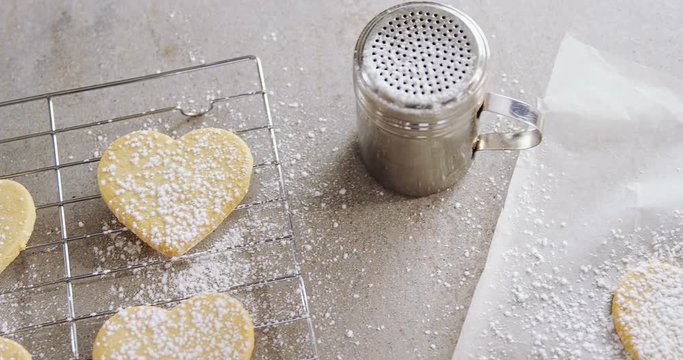 Raw heart shape cookies on baking tray with flour shaker strainer, cookie cutter and wax paper 