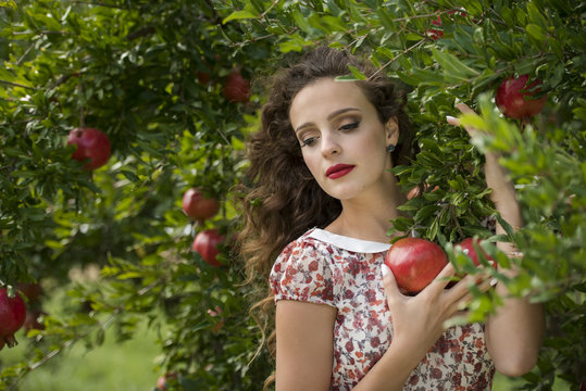 Young woman wearing floral long dress standing against pomegranate trees