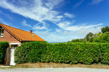 Fototapeta na wymiar Country house with green fence in the region of Normandy, France on a sunny day. Beautiful countryside, french lifestyle and typical french architecture, european country landscape.