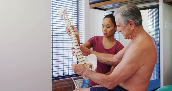 Physiotherapist explaining the spine model to senior patient 