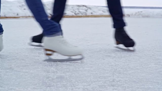 Tracking with low-section of legs of unrecognizable man and woman wearing jeans spinning on outdoor ice rink