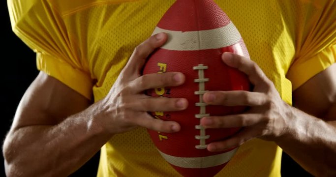 American football player holding ball against black background 