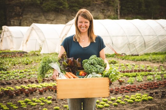 Portrait of smiling woman holding crate full of vegetables on farm