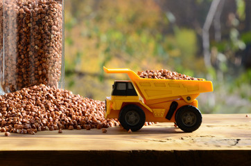 A small yellow toy truck is loaded with brown grains of buckwheat around the buckwheat pile and a...