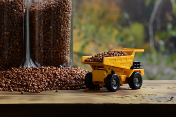 A small yellow toy truck is loaded with brown grains of buckwheat around the buckwheat pile and a...