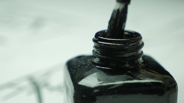 Detail of a chinese brush tip dipped in a reflective ink surface in black jar. Close up to brush and ink. Calligraphy brushes with chinese ink