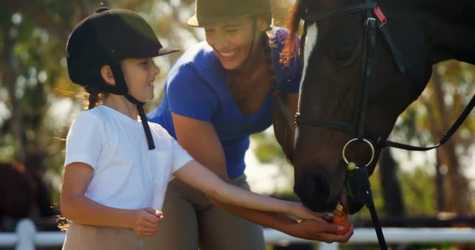 Happy mother and daughter feeding carrot to horse 