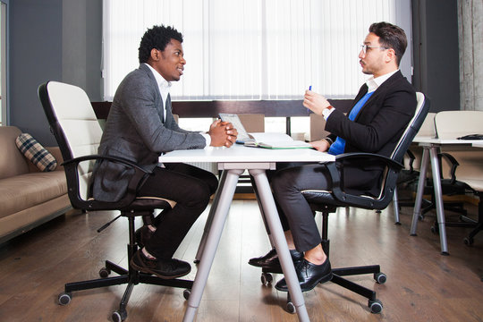 Two young businessmen, white desk, job interview, teamwork. Two successful male entrepreneurs at office work together