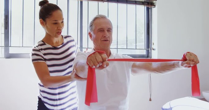 Mixed-race physiotherapist helping patient in performing exercise with resistance band 