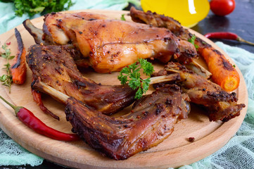 Fried pieces of rabbit with vegetables on a wooden tray on a dark background.